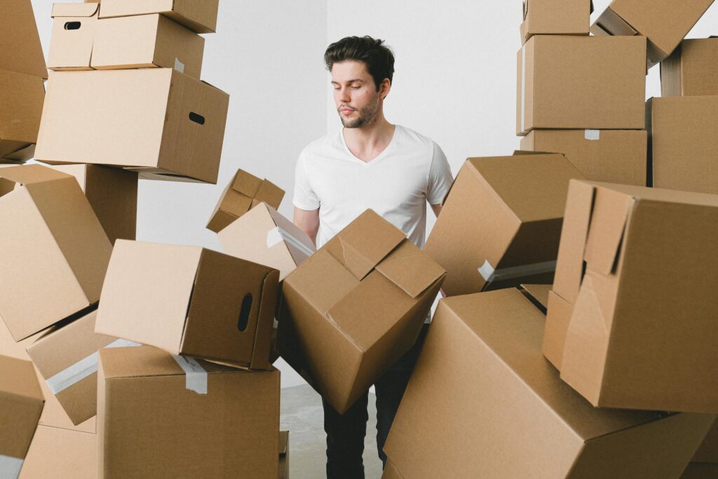 A young man surrounded by moving boxes indoors, contemplating unpacking.