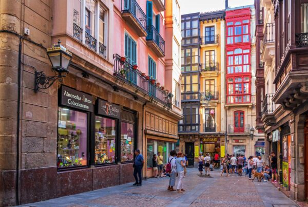 Bustling city street with colorful buildings and people enjoying a sunny day, showcasing urban life.